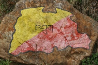 A map of Bhutan, painted in the colours of the national flag, on a rock beside a path to a monastery.